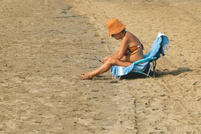 白天，穿着蓝色比基尼的女人坐在海滩上的蓝色折叠椅上